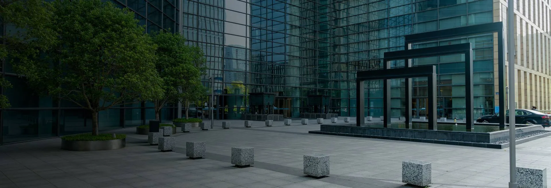 Modern office courtyard with blue glass facades, trees and white concrete cubes.